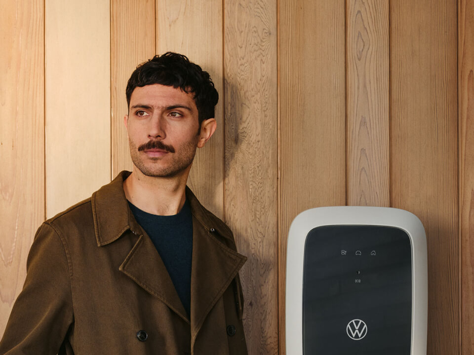 Chico mirando a la cámara apoyada sobre una pared ocre con un ID.Charger de Volkswagen